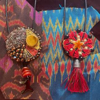 Photo of two colorful beaded pendant necklaces against a patterned background.