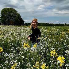 Young white woman in a field of wildflowers, spinning towards the camera.