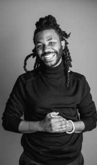 Cheerful young Black man with braided hair smiling brightly for the camera.