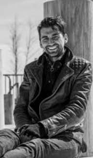 White man with short hair smiling broadly for the camera while sitting outside. 