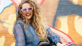 Artist Katie Stewart smiles in front of a mural