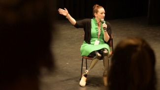 Photo of a woman wearing a green dress sitting on a chair holding a microphone