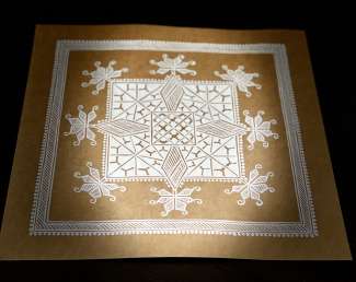 white ink in patterns on brown paper with a bright light on the center of the artwork