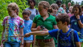 a group outdoors with child pointing at something with a stick