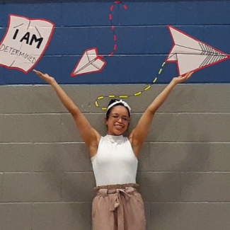 Artist Ciana Jackson smiling and holding up her hands in front of her mural. 
