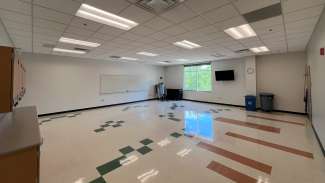 A medium sized classroom with multiple tables and chairs and a whiteboard 
