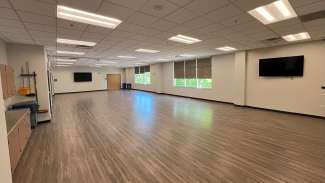 A large open multi-purpose room with a bulletin board and white board 