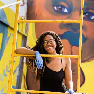 Artist Dare Coulter smiles at the camera on a ladder