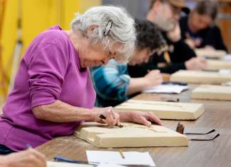 An artist participates in a workshop scratching their design in a block