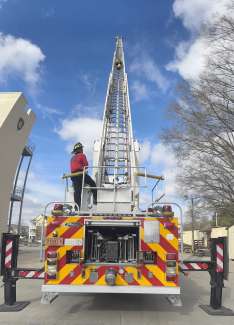 A laddar fire truck with a recruit climbing the tall ladder and an instructor standing next to the truck