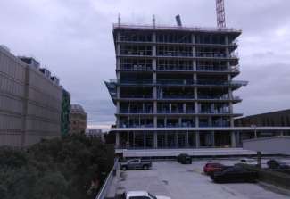 image of the new City Hall construction site taken on August 5, 2025, shows the building coming up over the parking deck and how it is taller than the Professional building across the street.  