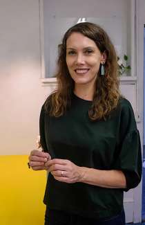 White female artist with long brown hair smiling and wearing jewelry of her own design. 