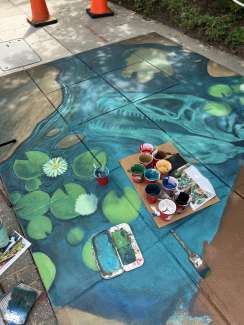 A sidewalk mural with green lillypads, and blue water and other nature scenes