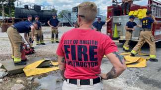 A fire instruction leader looks on as fire recruits practice opening a fire hydrant