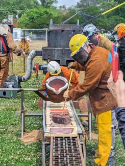 A man in fire protective gear pours molten iron from a furnace into molds