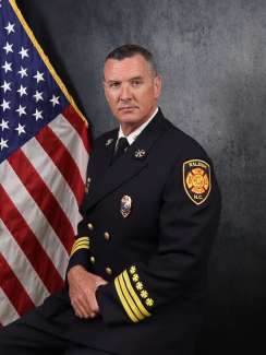 A portrait of Division Chief Preston Gaster from the Raleigh Fire Department. An American flag is part of the backfrop