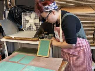 Artist working in a studio making green paper using a screen and pulp. 