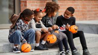 children in costumes sitting on the stairs with orange pumpkin containers