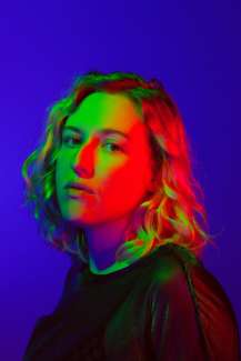 The artist looks into the camera while red and green lights shine on her face