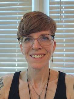 The poet smiles into the camera. They have short hair and glasses.