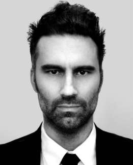 A man with dark hair looks at the camera.