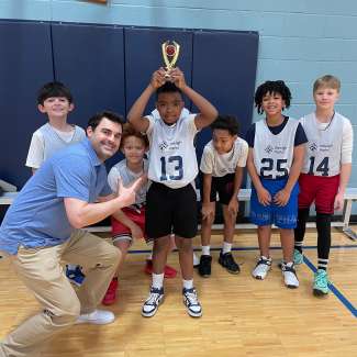 a child smiling with their teammates and a trophy for winning the sportsmanship award