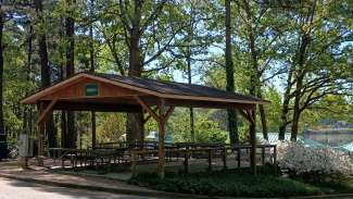 a shelter with trees, flowers and a lake in the background