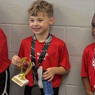 a child smiling with a trophy for winning the sportsmanship award