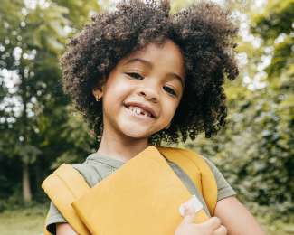a child smiling holding a notebook with a bookbag on