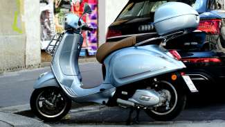 A moped parked behind a car by a curb