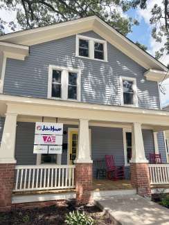 A light blue house with a yellow door and pink rocking chairs