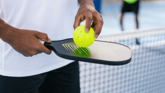 Person holding a pickleball paddle and ball