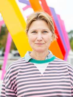 A woman in a striped shirt stands in front of colorful poles